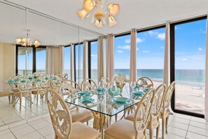 A dining area with a glass table and chairs, large windows with a view of the beach, and a ceiling light fixture. - Oh Buoy! Catch the Breeze at This Beachfront Escape! Sleeps 8! (Panama City Beach)