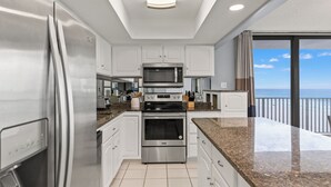 A modern kitchen with stainless steel appliances, white cabinetry, and a view of the ocean through large windows. - Buoy Oh Buoy! Sun, Sand, and Smiles Await! Sleeps 8! (Panama City Beach)