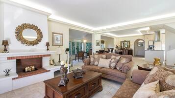 A spacious living room with a fireplace, a large sofa, and a dining area in the background.