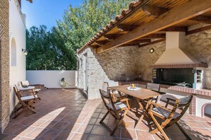 An outdoor patio with a stone wall, wooden furniture, and a built-in grill. - Villa Melia Athenian Riviera (Vari - Voula - Vouliagmeni)