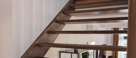 Un escalier moderne avec des finitions en bois, menant à un niveau inférieur où se trouve un coin repas.