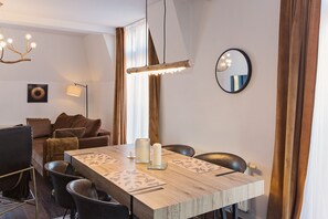 Un comedor con una mesa de madera, sillas, una araña, un espejo y un sofá.