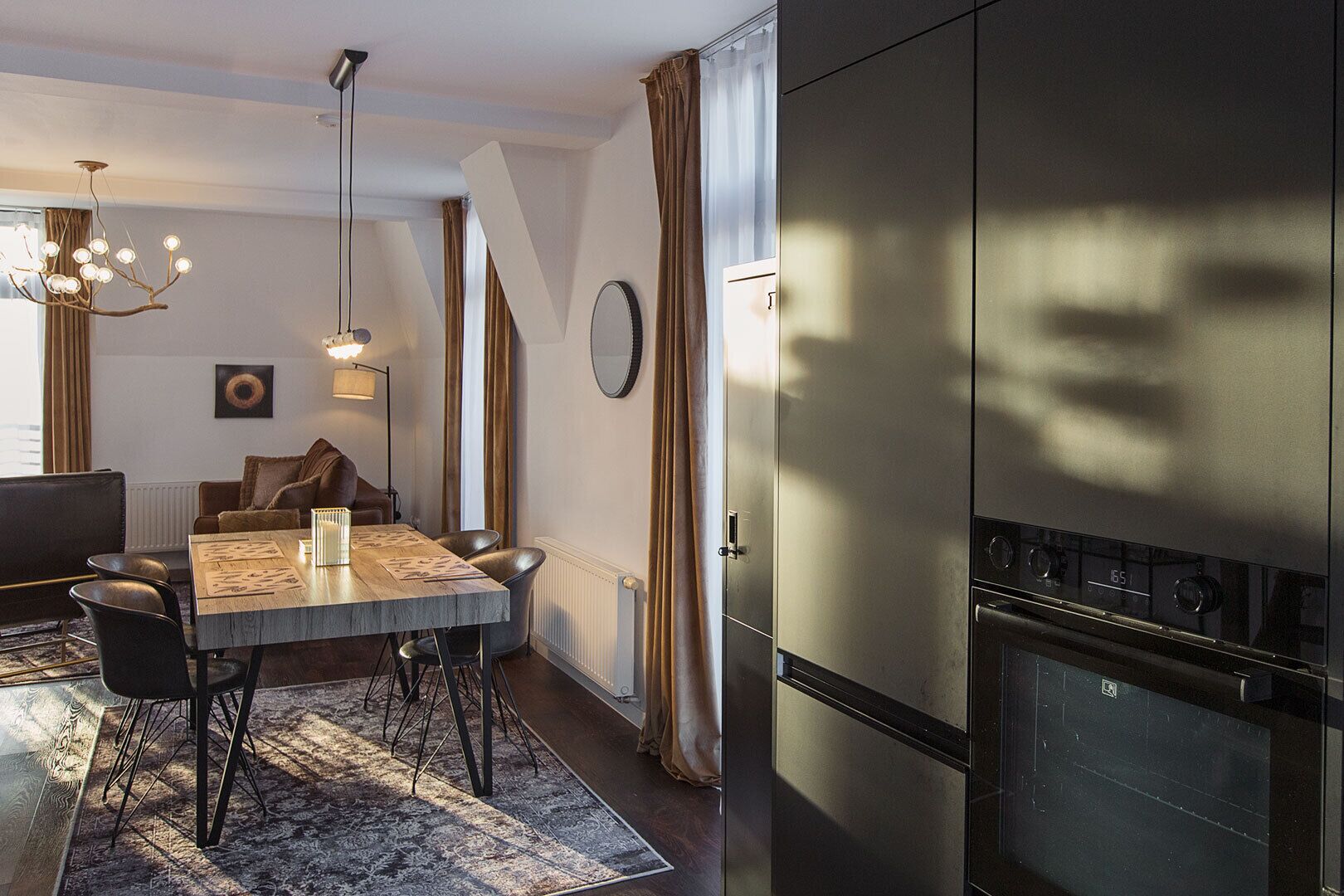 A modern kitchen with a built-in stove, a dining area with a wooden table and chairs, and a chandelier.