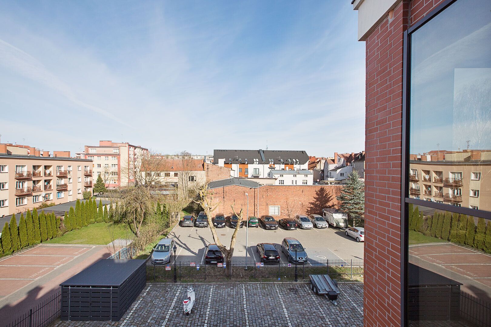 A view of a parking lot with multiple cars, a brick building, and residential buildings in the background.