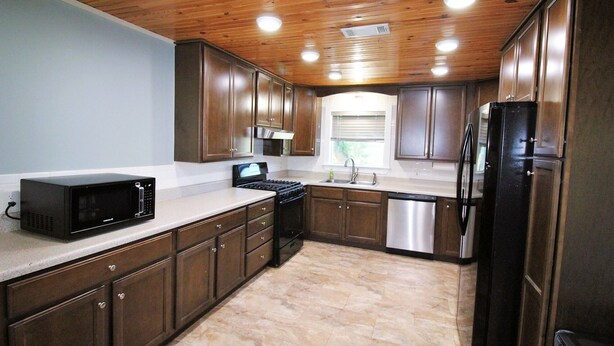 Una cocina con armarios de madera, microondas, estufa, lavaplatos y pileta.