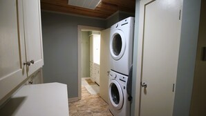 Un lavadero con dos lavadoras apiladas, una encimera blanca y un pasillo que conduce a otra habitación.