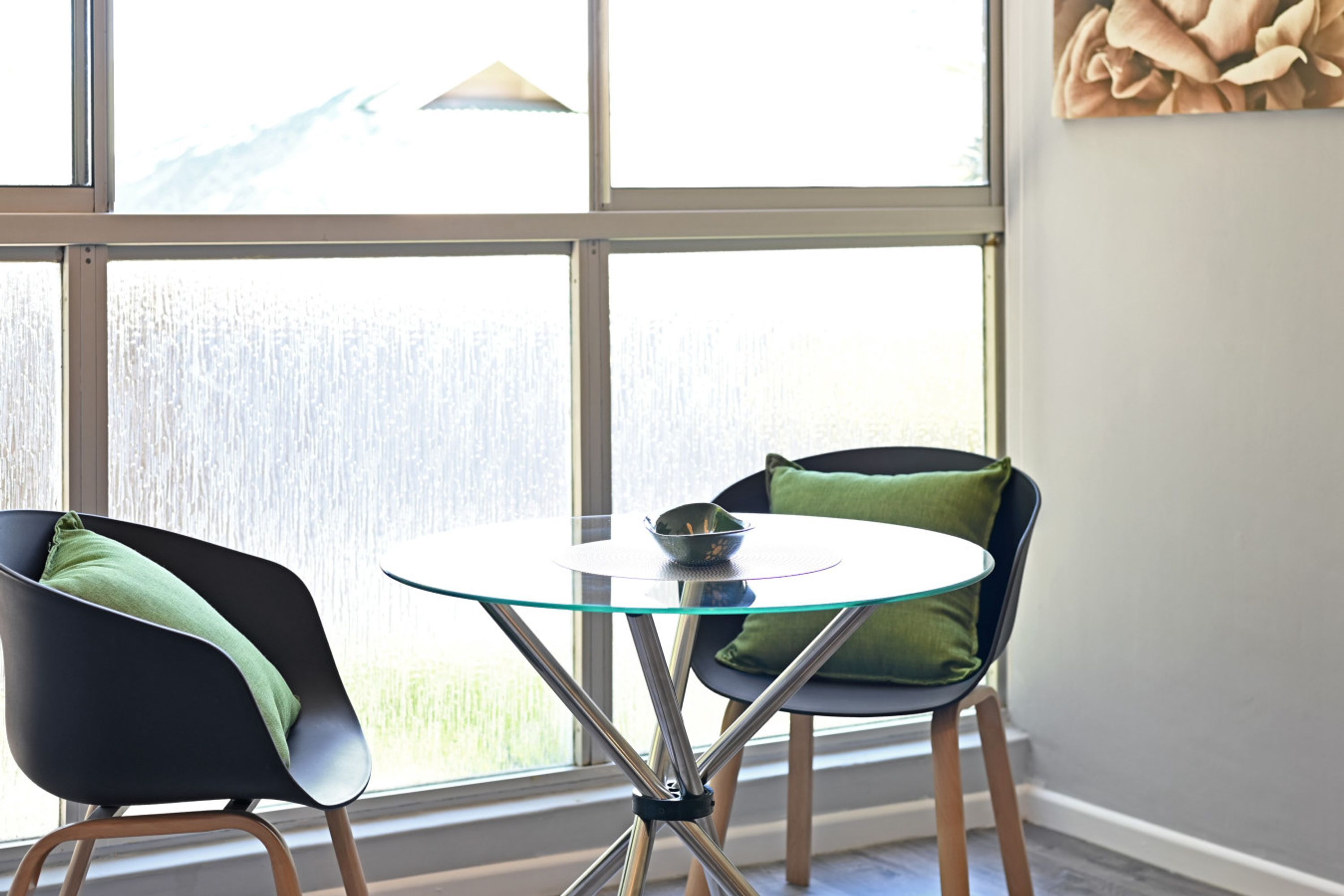 A room with a glass table and two chairs with green cushions.