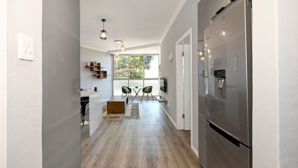 A modern kitchen with a stainless steel refrigerator, wooden flooring, and a dining area with a table and chairs. - Modern Two Bed Central Green Point Stadium (Cape Town)