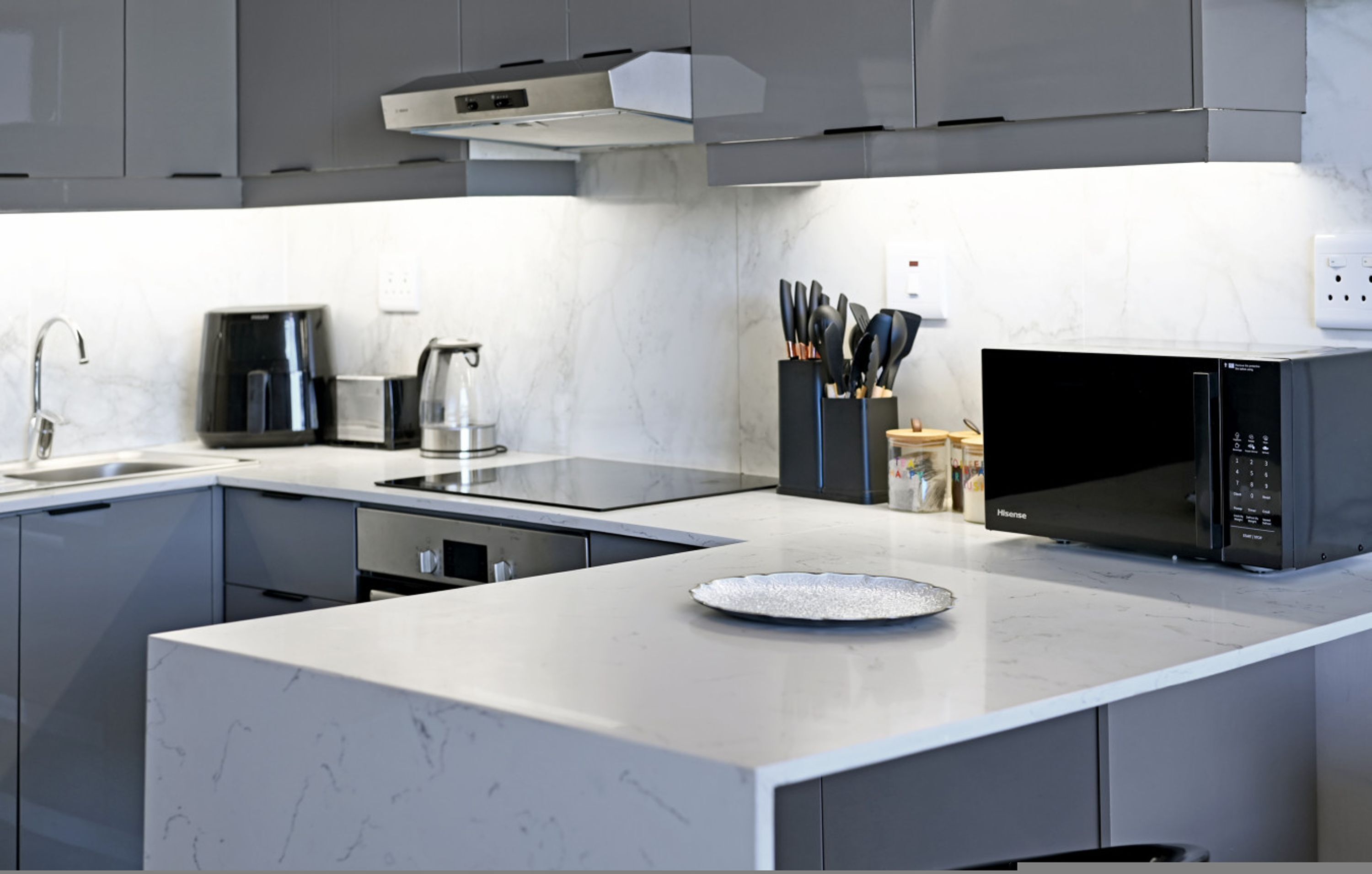 Una cocina moderna con gabinetes grises, un microondas negro, una cafetera y un bloque de cuchillos.