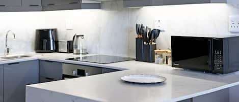 Una cocina moderna con gabinetes grises, un microondas negro, una cafetera y un bloque de cuchillos.