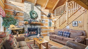 Interior acogedor de una cabaña de madera con chimenea, paredes de madera, una escalera y muebles rústicos.
