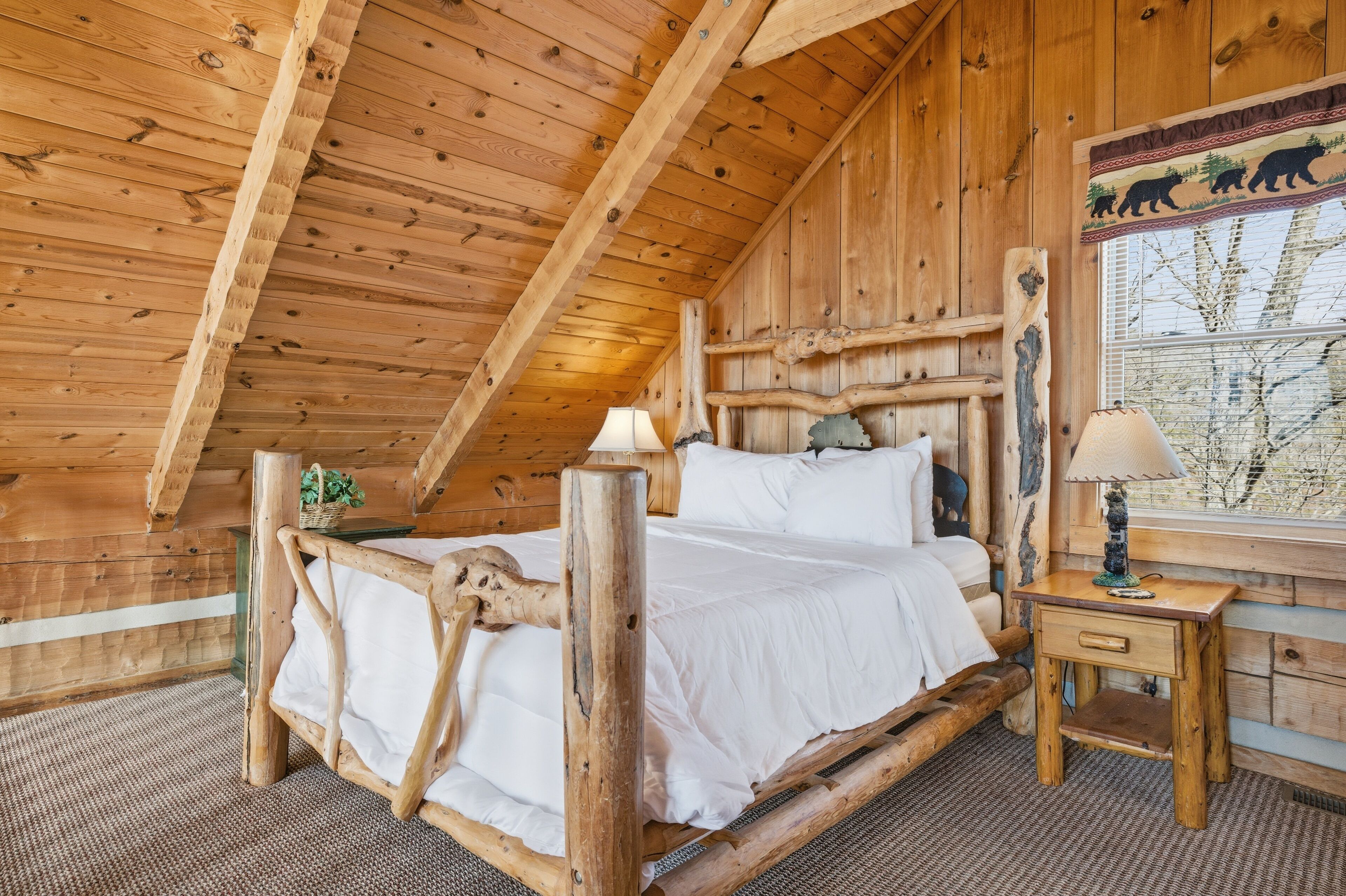 A wooden cabin room with a bed, a nightstand, and a window with a bear decoration.