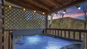 Un jacuzzi bajo una pérgola de madera con fondo de celosía y luces colgantes.