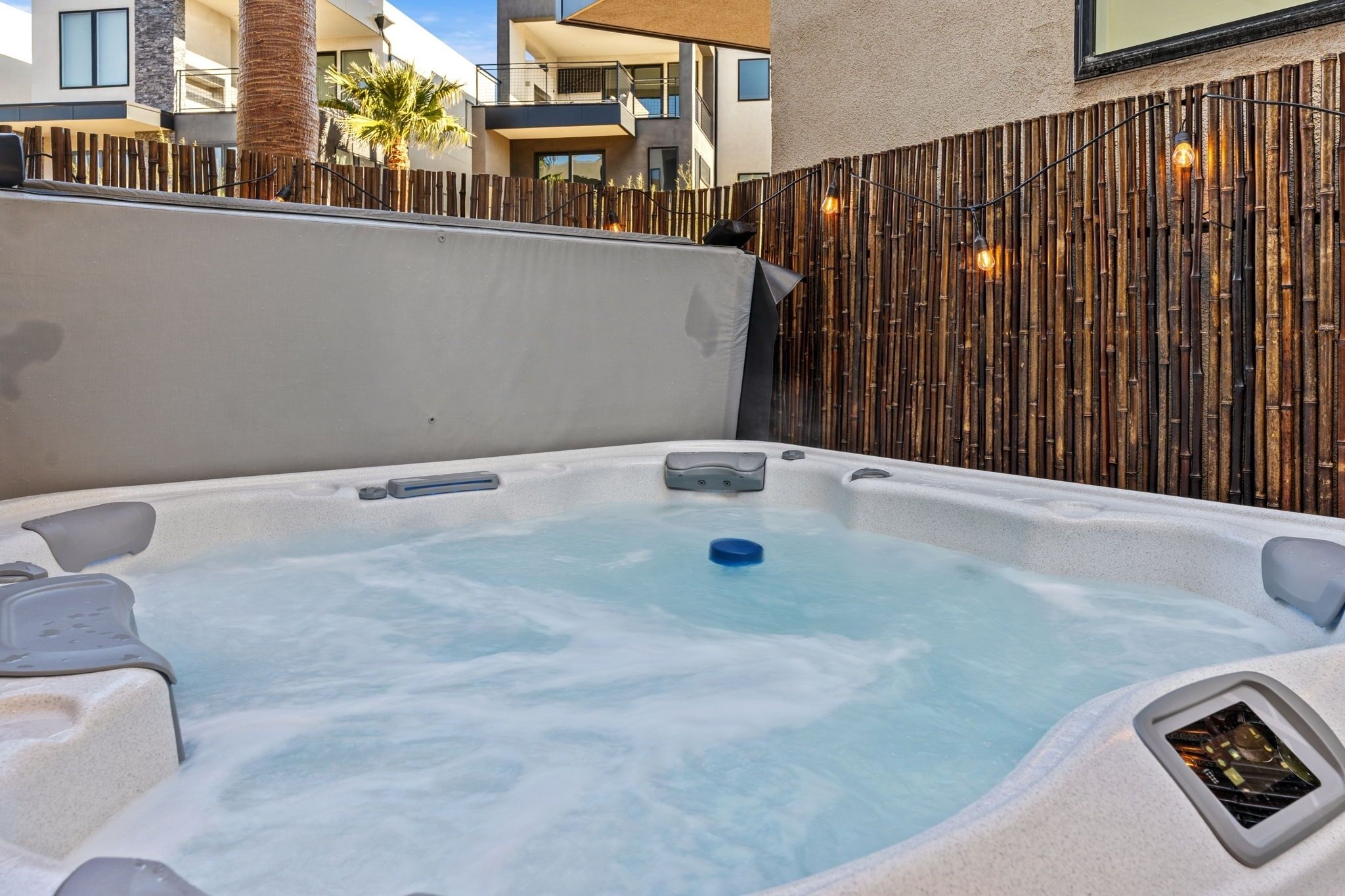 A hot tub with a bamboo fence and a view of modern buildings.