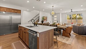 A modern kitchen with a stainless steel refrigerator, wooden cabinets, and a marble island. - Simply Paradise 5 Bedroom Townhouse (St. George)
