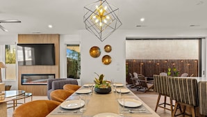 A modern dining area with a long table set for six, a flat-screen TV above, and a decorative plant centerpiece. - Simply Paradise 5 Bedroom Townhouse (St. George)