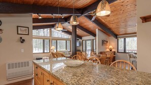 Une cuisine spacieuse dotée de plans de travail en granit, d’armoires en bois et d’un grand îlot central. On y trouve plusieurs luminaires suspendus et un ventilateur de plafond.