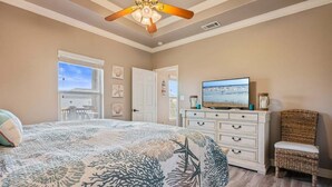 Ein Schlafzimmer mit einem Bett, einem Fernseher, einem Schminktisch, einem Sessel und einem Deckenventilator.