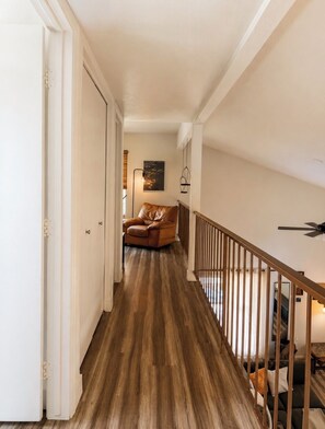 Ein Korridor mit Holzboden, einem Ledersessel, einem Deckenventilator und einer Treppe mit Holzwand.