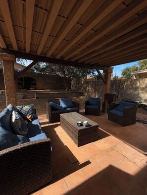 Eine Terrasse im Freien mit Korbmöbeln, einem Couchtisch und einer Grillgelegenheit.