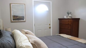 A bedroom with a bed, pillows, a dresser, and a door.