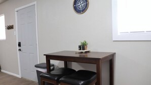 A room with a wooden table and two black leather chairs, a white door, a compass wall decoration, and a small potted plant on the table.