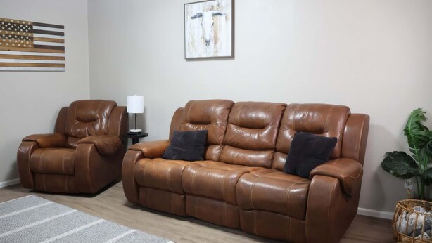 A living room with two brown leather sofas, a small side table, a lamp, a large American flag, and a painting on the wall.
