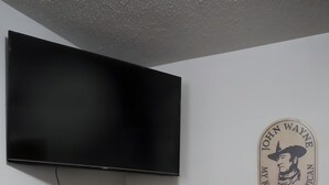 Et værelse med et fladskærms-tv på væggen, et rundt bord med tre stole og en logo på væggen.