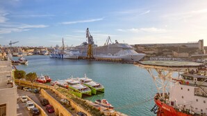 Un grand navire de croisière était amarré à un port, à proximité duquel se trouvaient une grue et de plus petits bateaux.