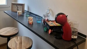 A modern kitchen with a black countertop, wooden stools, a red kettle, and framed pictures on the wall. - Between lakes and mountains (Cluses)