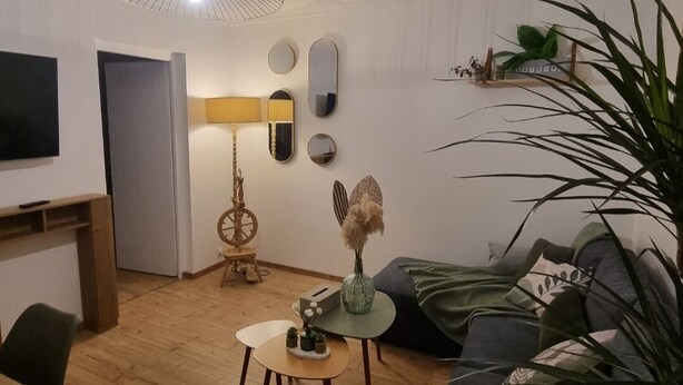 A modern living room with a wooden floor, a round coffee table, a sofa, and a large plant. - Between lakes and mountains (Cluses)