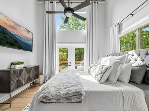 Ein Schlafzimmer mit Bett, Deckenventilator, Fernseher, Fenster und Blick ins Freie.