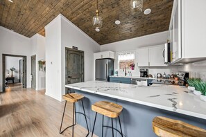 Eine moderne Küche mit einer großen Kochinsel, Holzbarhocker und einer rustikalen Decke.