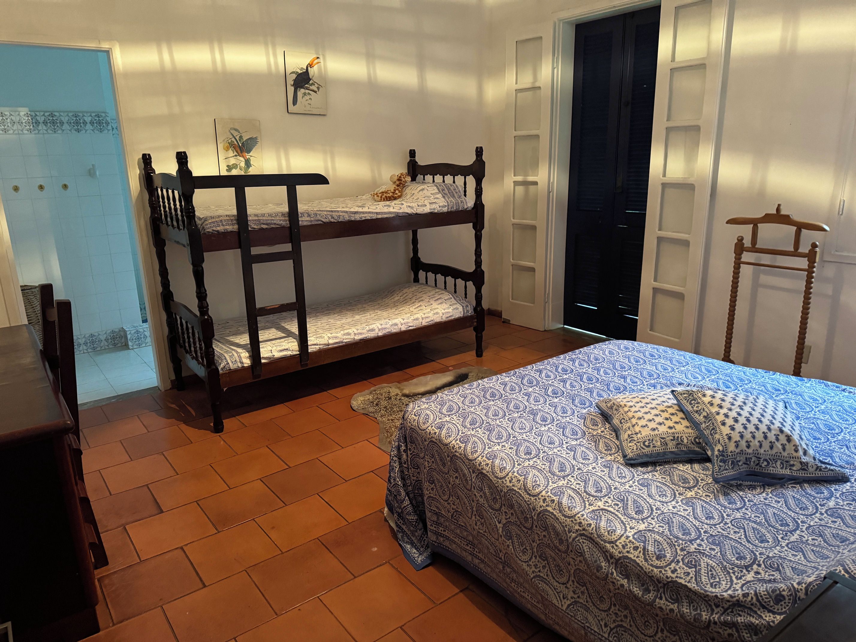 Una habitación con literas, una cama individual con ropa de cama estampada, una silla de madera y una puerta.