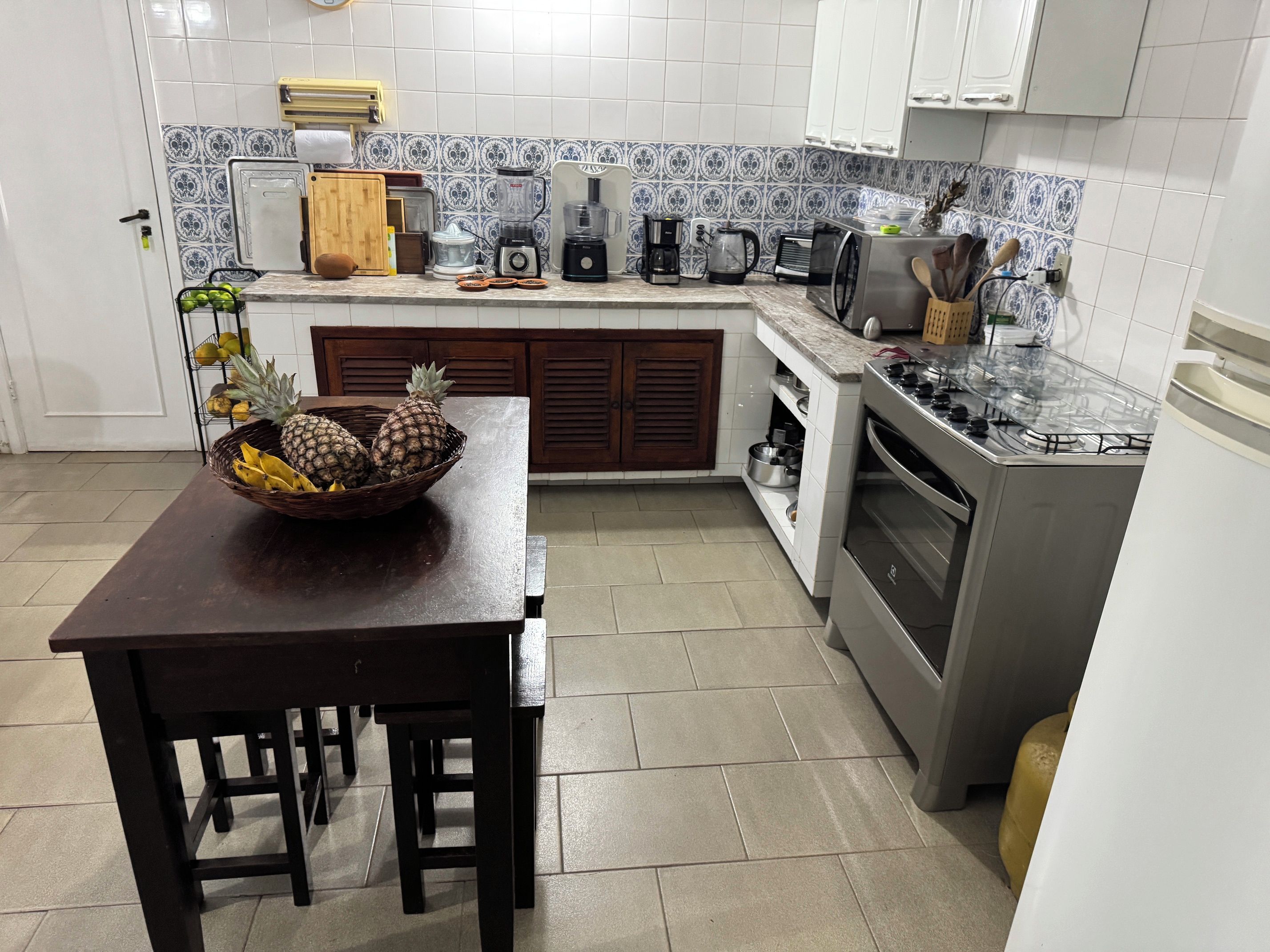 Una cocina con una mesa de madera, un cuenco de fruta, una estufa y varios electrodomésticos.