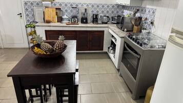 Una cocina con una mesa de madera, un cuenco de fruta, una estufa y varios electrodomésticos.