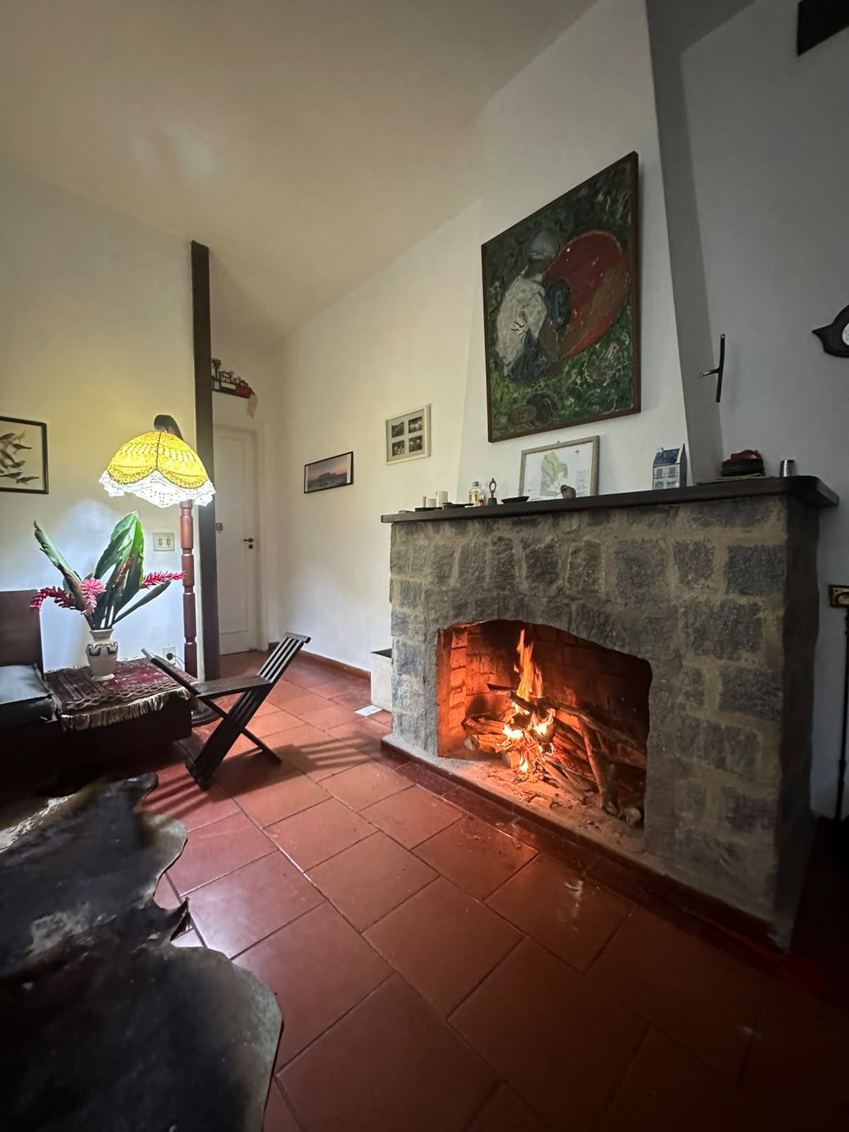 A living room with a stone fireplace, a lamp, and a painting on the wall.