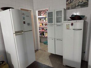 Una cocina con armarios blancos, un refrigerador y un congelador. Cuenta con un salpicadero de azulejos y una cesta en la pared.