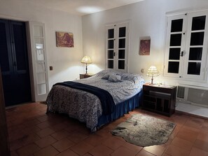 Een slaapkamer met een bed, twee bedlampen, een vloerkleed en een raam met jaloezieën.