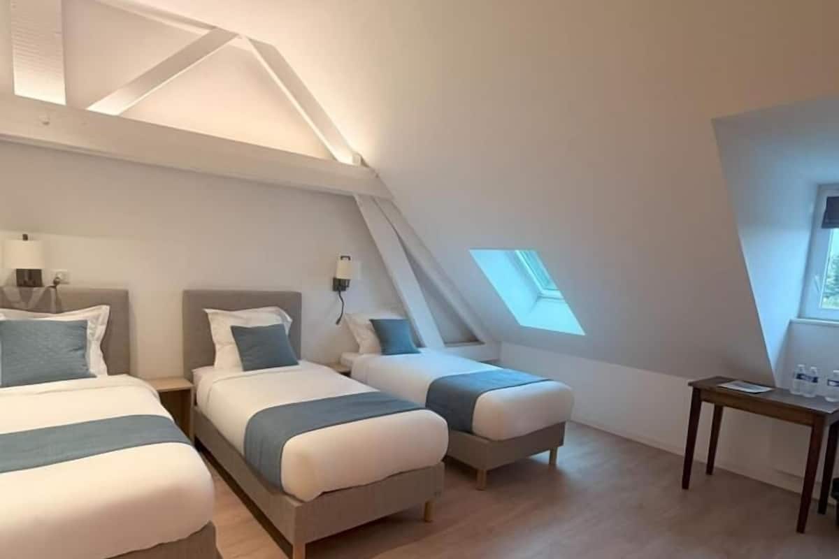 Una habitación moderna y amplia con dos camas, una mesita y tragaluces.