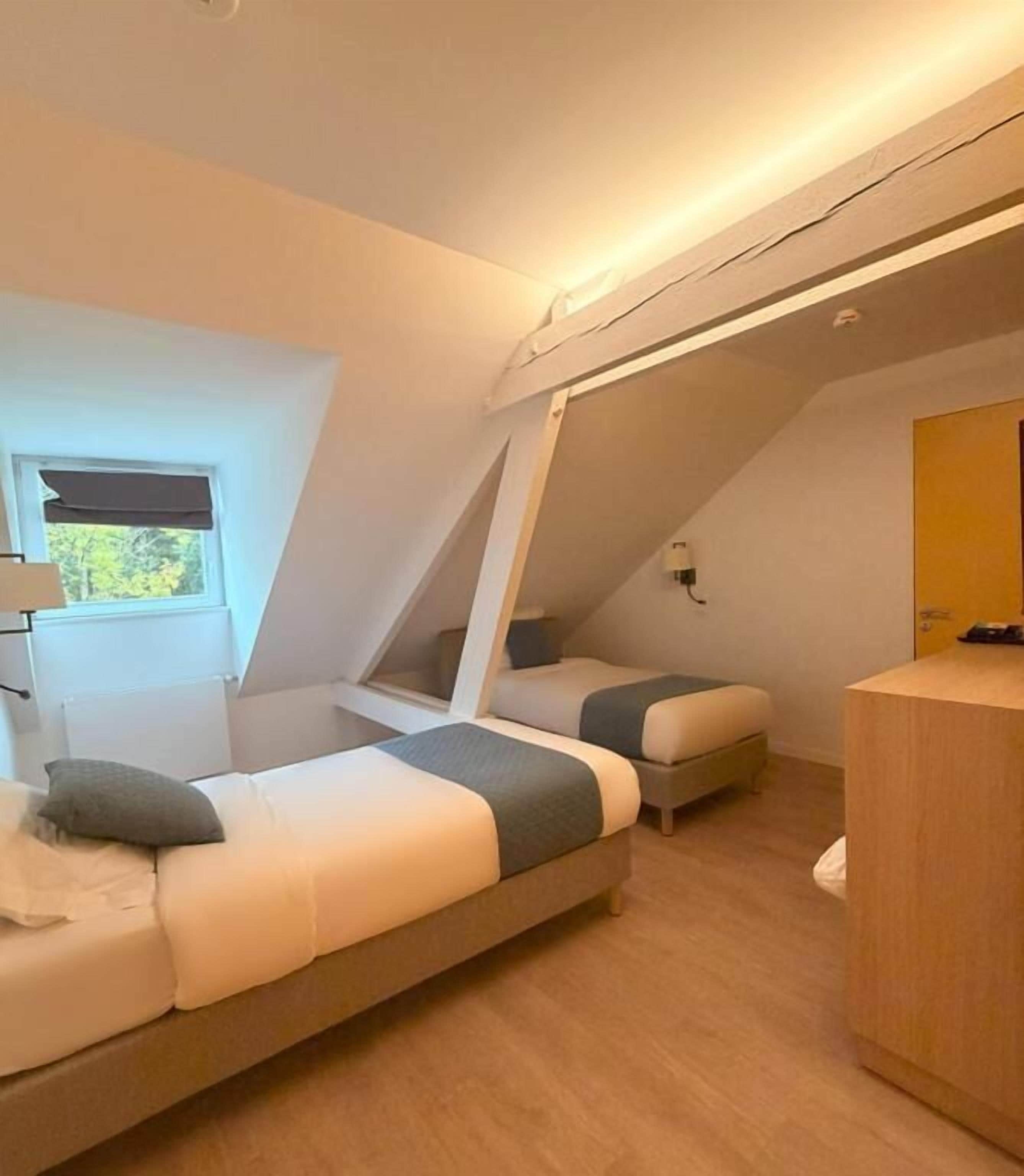 Une chambre compacte et moderne, équipée de deux lits superposés, d’un petit bureau et d’une fenêtre donnant sur la verdure.
