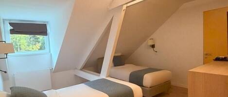 A compact, modern room with two bunk beds, a small desk, and a window with a view of trees.