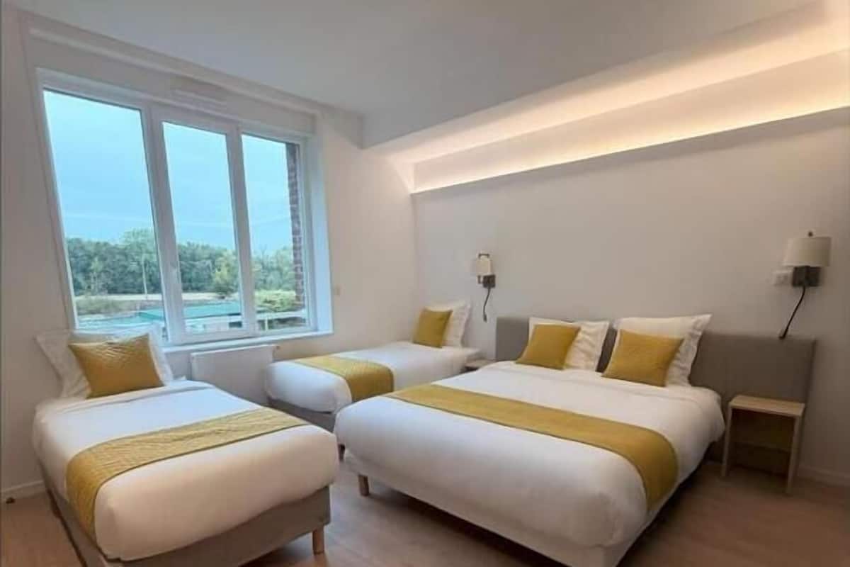 Una habitación de hotel moderna con tres camas, ventanas amplias y vistas a zonas verdes.