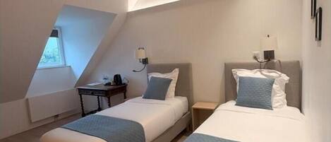 A modern hotel room with two beds, a small desk, and a window.