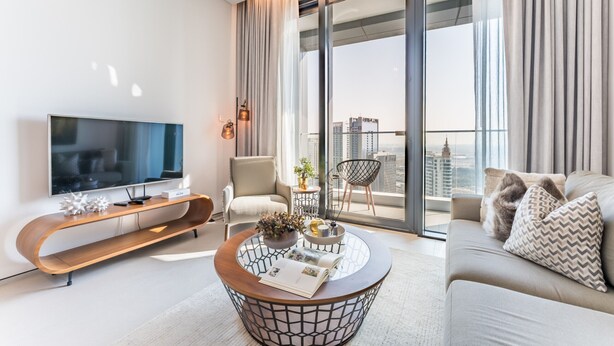 A modern living room with a flat-screen TV, a wooden console table, a round coffee table, a sofa, and a balcony with a city view. - Balcony Facing the Marina with Partial Sea Views, Steps from the Beach (Dubai)