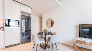 A modern kitchen with a dining area, featuring a round table with chairs, a round mirror, and a wooden console table with decorative items. - Balcony Facing the Marina with Partial Sea Views, Steps from the Beach (Dubai)