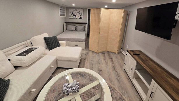 A modern, compact living space with a bed, sofa, TV, and a small table. - Cozy East Hill 2026! (Belleville)