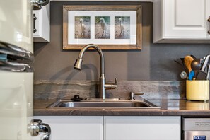 A kitchen with a stainless steel sink, a framed picture of birds, and a utensil holder. - Aldea 1, Belleair Beach, 2BR,2BA (Belleair Beach)