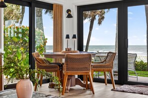 Uma sala de jantar com cadeiras de vime, uma mesa redonda e vista para o oceano.