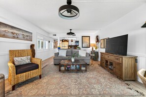 Ein Wohnzimmer mit Sofa, Korbsessel, Couchtisch, Fernseher und Schrank.